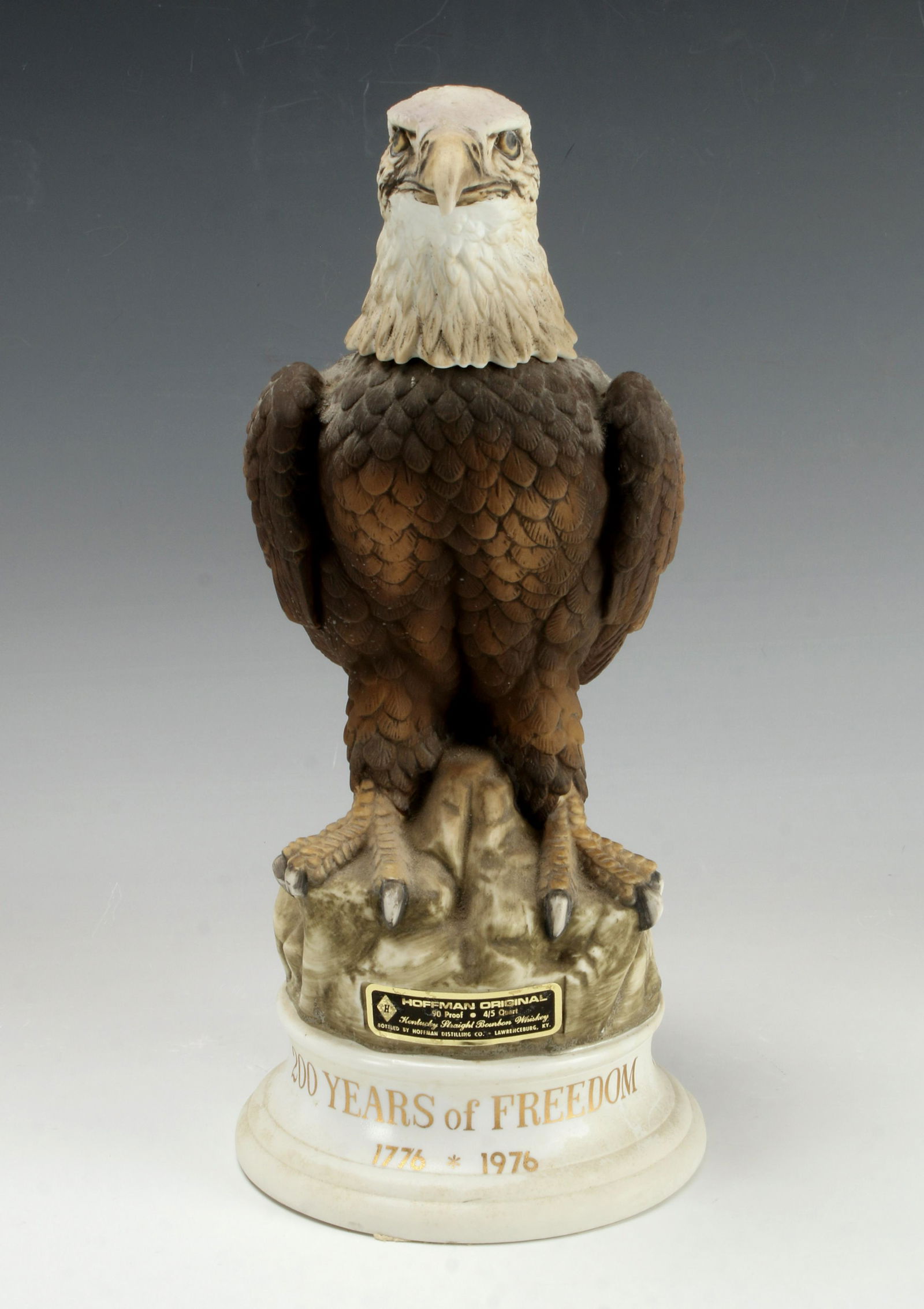 EAGLE BICENTENNIAL HOFFMAN DECANTER MUSIC BOX: EAGLE BICENTENNIAL HOFFMAN DECANTER MUSIC BOX A bald eagle is perched on a cliff. Head lefts off. Music box on bottom. Marked Hoffman Original 1974 on back.