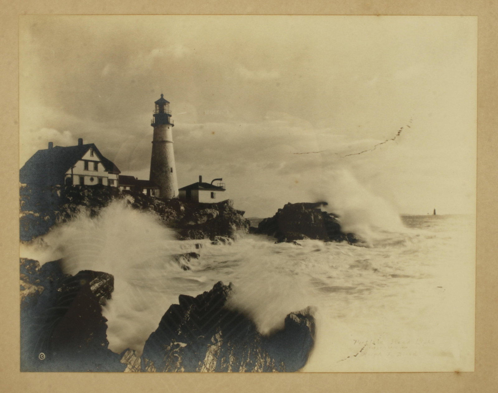 PHOTOGRAPH PRINT OF LIGHTHOUSE: PHOTOGRAPH PRINT OF LIGHTHOUSE Signed Portland Head Light, Ralph F. Blood 1931. Black and white photograph print, lighthouse sits on seaside cliffs as ocean spray breaks over the cliff w