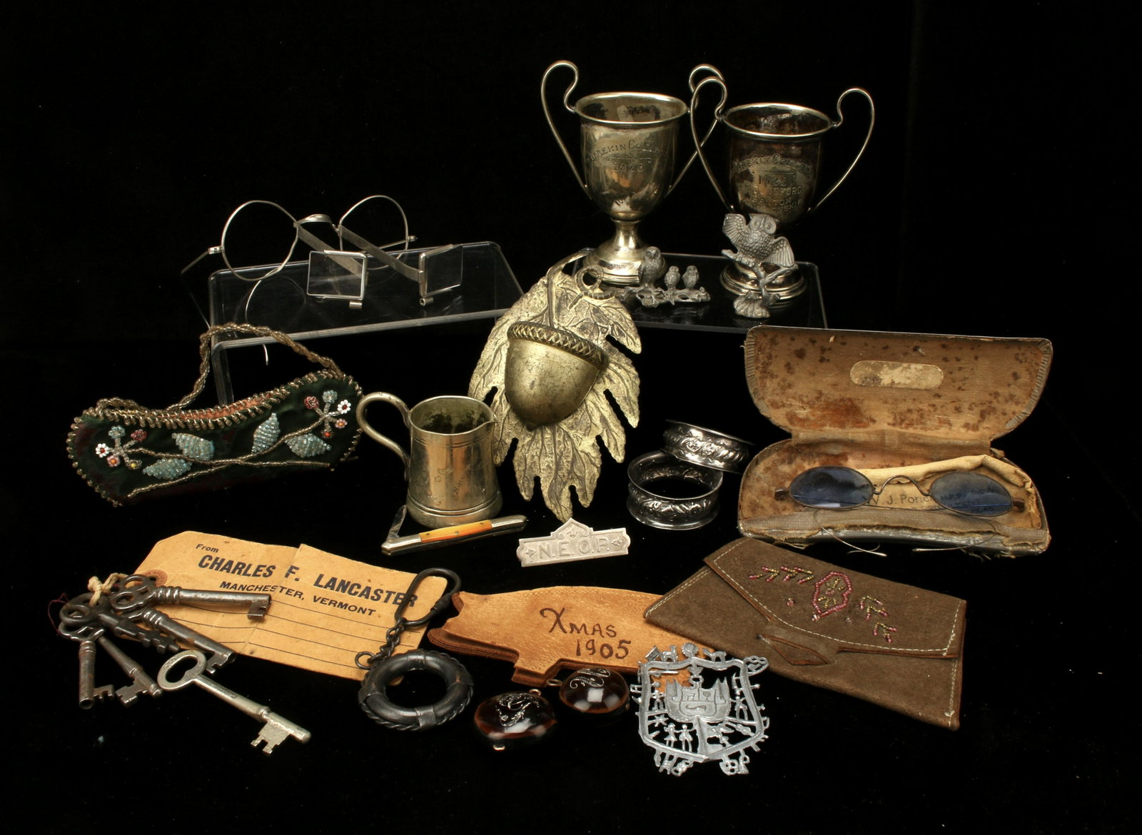 ASSEMBLED LOT VINTAGE MEMORABILIA KEY SPECTACLES: ASSEMBLED LOT VINTAGE MEMORABILIA KEY SPECTACLES Small silverplate trophies (1925, 1926, 1935), magnifying spectacles, napkin rings, initial pendants made of island nut, leather Christma