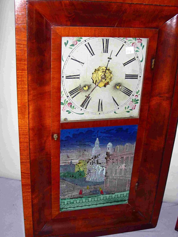 Ogee Clock of Philadelphia Interest: A mahogany veneer 30 hour ogee clock by New Haven, attributed to Chauncey Jerome and with a label printed by Hiram and a reverse painted glass of Independence Hall.