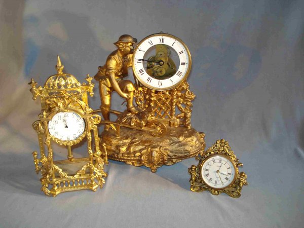 Three Clocks: Three clocks: A cast gold gilt metal desk clock with an 8 day round white porcelain dialed timepiece, 7" in height; a gilt metal desk or mantel clock with skeletonized movement and showing a man with 