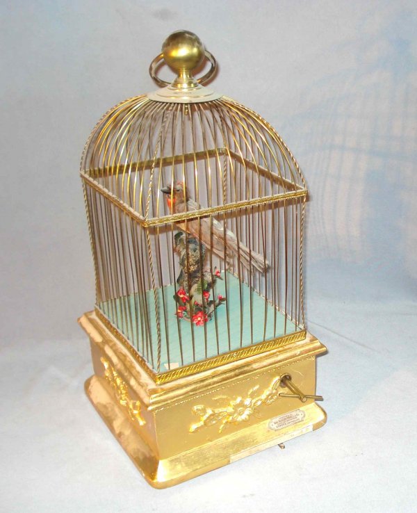 Swiss Singing Caged Bird : A feathered mechanical bird within a 19" X 10" square cage with a gilt wood base. In the base is a label "Chevob & Co. (the late Baker Troll Co. of Geneva)".