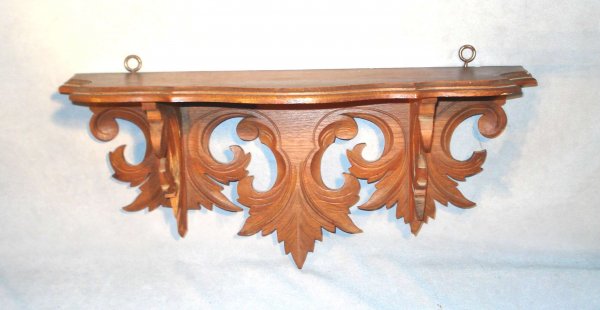 Carved Walnut Clock Shelf: A carved shelf with a base carved in a leaf-like pattern and with shaped top, 7" deep tapering to about 5" and 19" long.