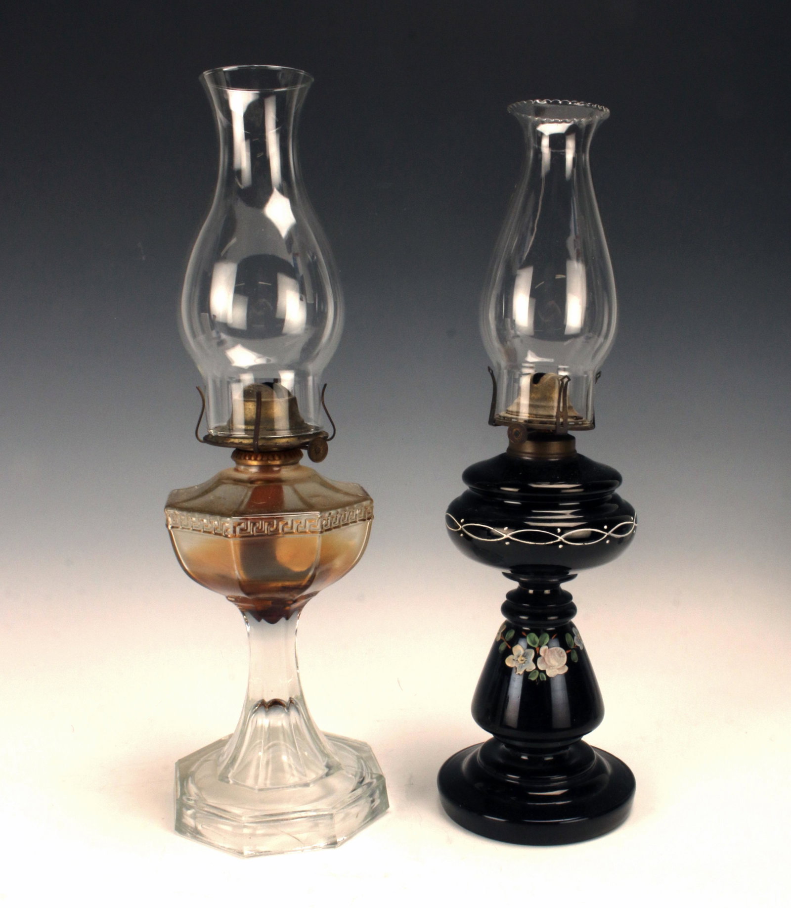 TWO ANTIQUE GLASS OIL LAMPS: TWO ANTIQUE GLASS OIL LAMPS One is clear pressed octagonal glass, the other has black glass with hand painted flower. Metal fitting on black glass lamp is marked Anne Queen.