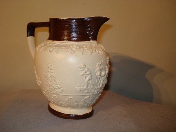 Bisque pitcher: A ironstone or bisque ware pitcher with a surround bas relief, having a brown glazed footing and top section, with a stamp on the bottom "Turner", perhaps for the late 19th century English potters of 
