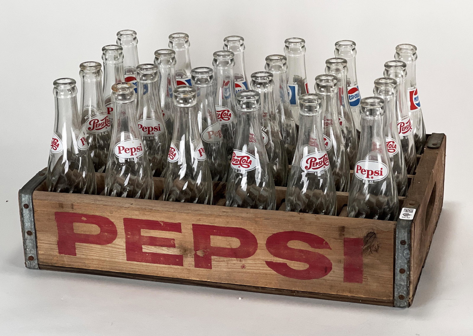 GLASS PEPSI BOTTLES IN WOODEN CRATE: GLASS PEPSI BOTTLES IN WOODEN CRATE 24 - 8 oz Glass Pepsi bottles with 2 different designs in wooden Pepsi crate. *one bottle has chip 18 1/2"