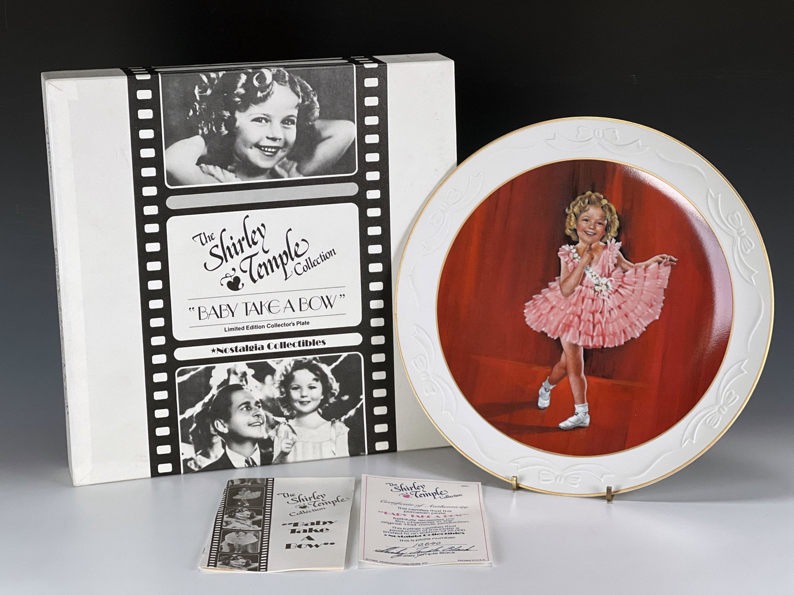 THE SHIRLEY TEMPLE BABY TAKE A BOW PLATE IN BOX: THE SHIRLEY TEMPLE BABY TAKE A BOW PLATE IN BOX Shirley Temple in that famous pink dress from Baby Take a Bow. Plate marked on back with number. Includes certificates and box.