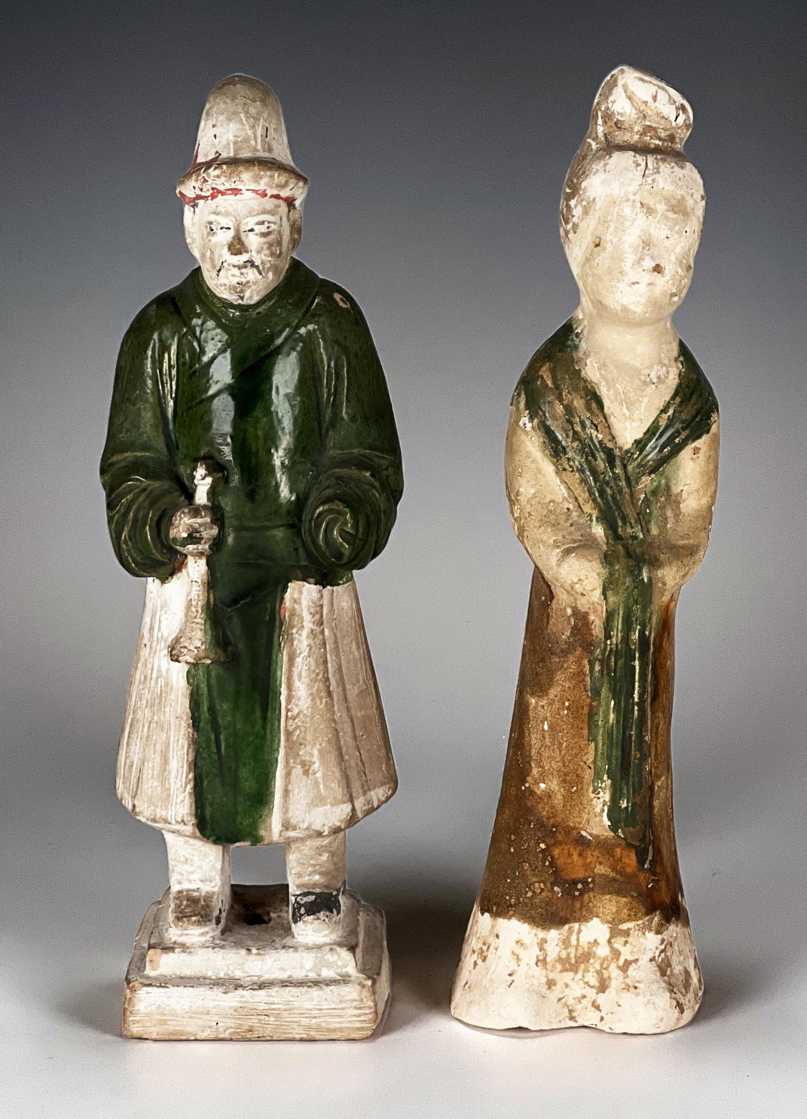 TWO TANG GLAZED FIGURES: TWO TANG GLAZED FIGURES Male and female. In a traditional green and yellow tang glaze on accenting unglazed clay. She is robed. He is holding a horn. Provenance: From the colle