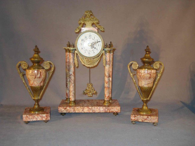 Clock garniture set: Decorate your mantel with this attractive clock set. A matching French made garniture clock set featuring a pillar or portico form clock with ormolu mounts and two matching urn style garnitures. Early