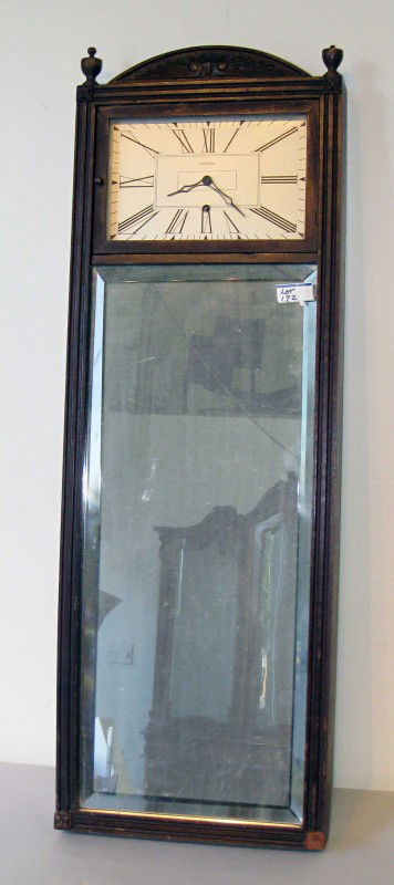 Mirror wall clock by Ansonia: A mahogany cased mirror clock with the clock mounted above a mirror. Balance wheel clockworks and whose silvered dial is signed "Ansonia".