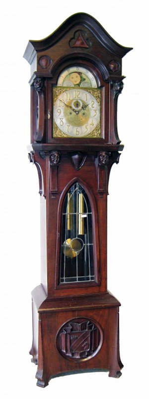 Fine Chime Hall Clock: A tubular chime hall clock whose clockworks, signed by the Herschede clock company, has an especially fine carved case featuring carved masks, corbel style, supporting the bonnet and tympanum. With a 