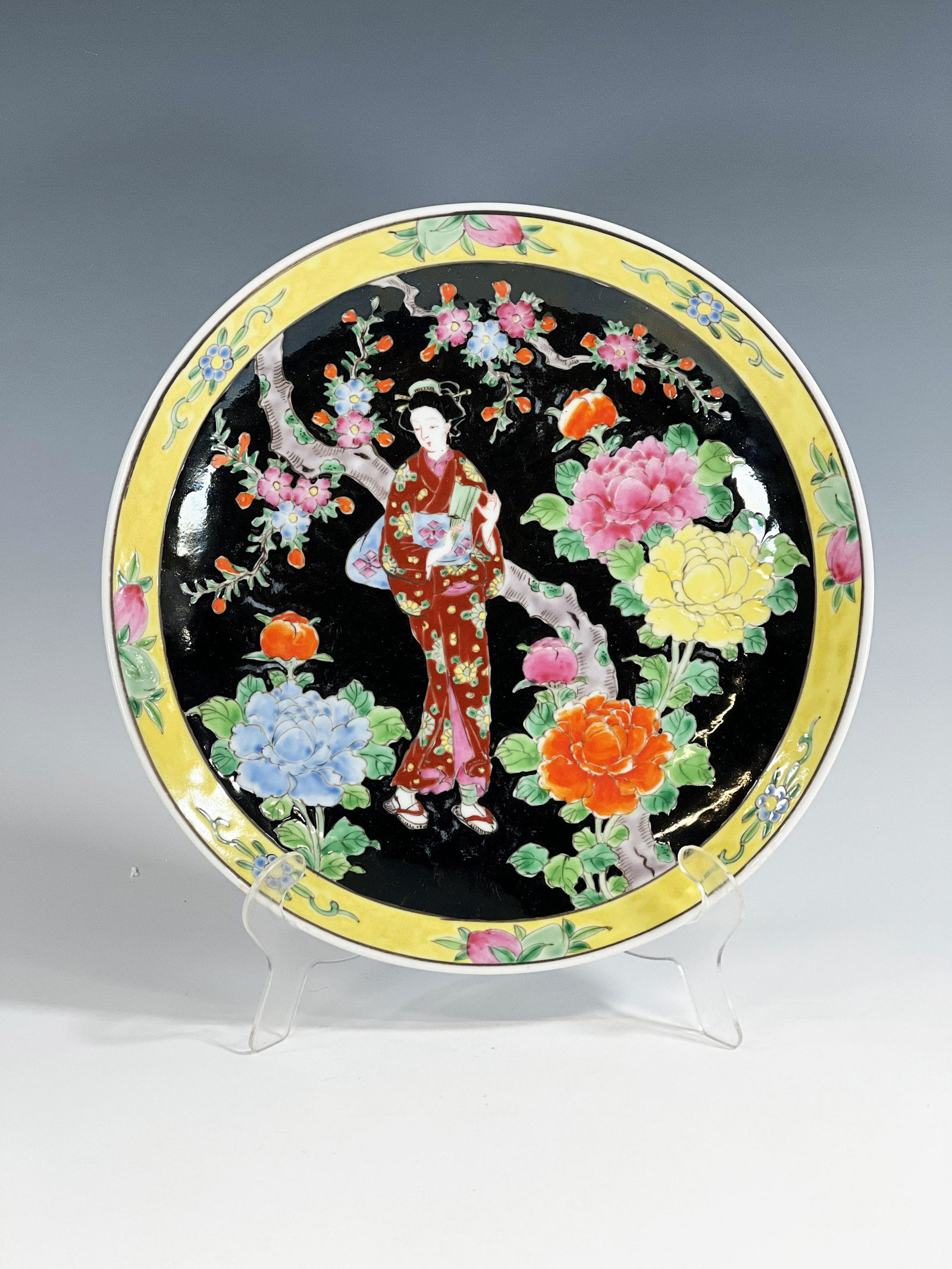 CHINESE PORCELAIN PLATE WITH BEAUTY IN A GARDEN: CHINESE PORCELAIN PLATE WITH BEAUTY IN A GARDEN A robed beauty stands in a garden among colorful flowers on a black ground. Yellow rim with floral decorations.