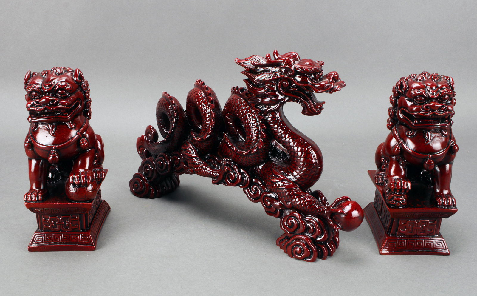TWO FOO BEASTS AND DRAGON STATUES: TWO FOO BEASTS AND DRAGON STATUES Red resin figures of a dragon clutching a pearl, and pair of foo dogs. 12" X 7" Shipping:</