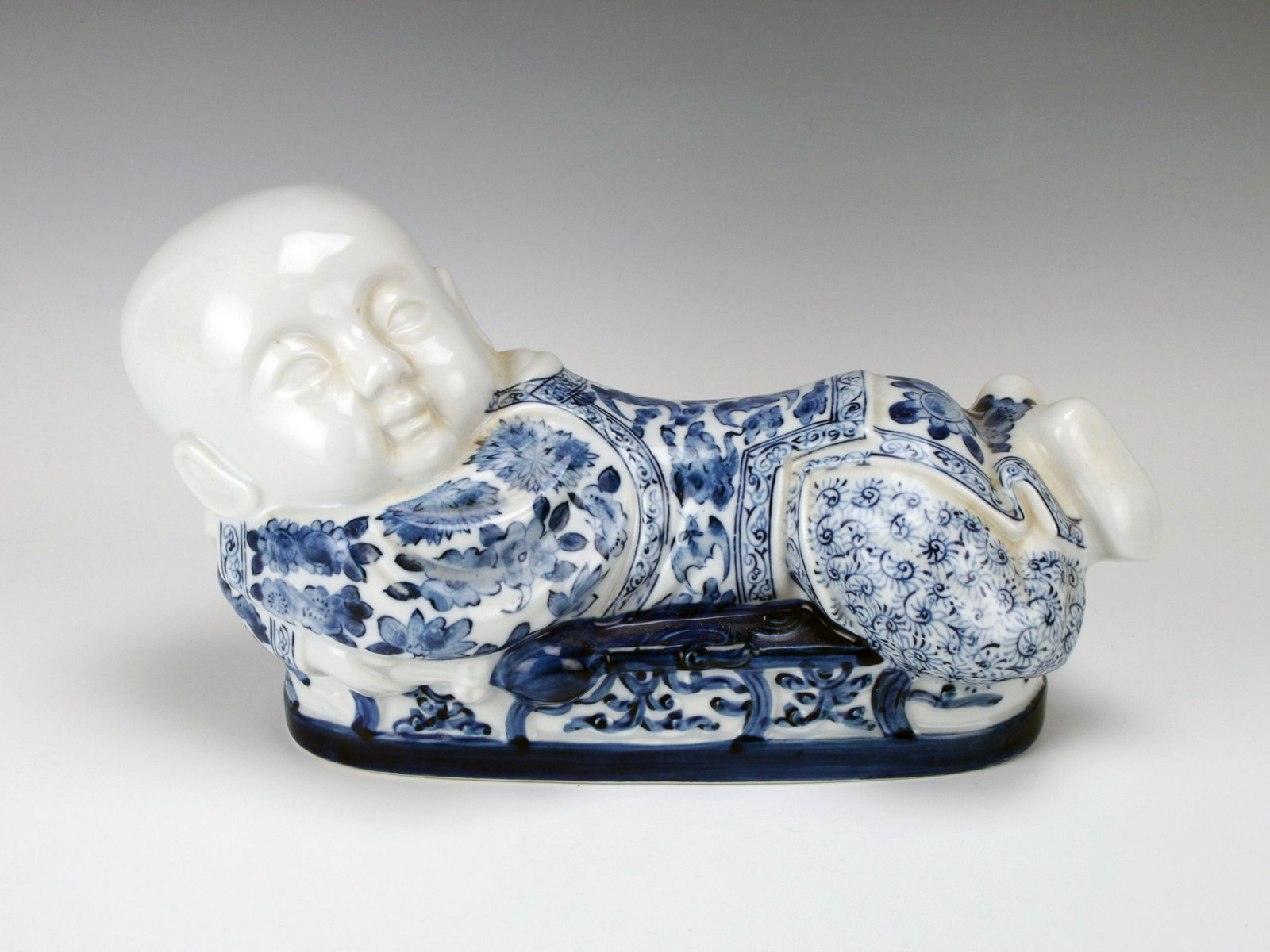 BLUE & WHITE PORCELAIN BABY HEAD REST: BLUE & WHITE PORCELAIN BABY HEAD REST Head rest in the shape of a child decorated in blue flowers and bat designs. 12" X 6"