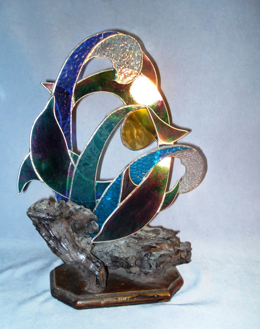 Glass Sclupture: A free form cut glass sculpture with different colored glasses mounted onto a driftwood base, with the theme of dolphins in the ocean. Signed on the base Janet Starr