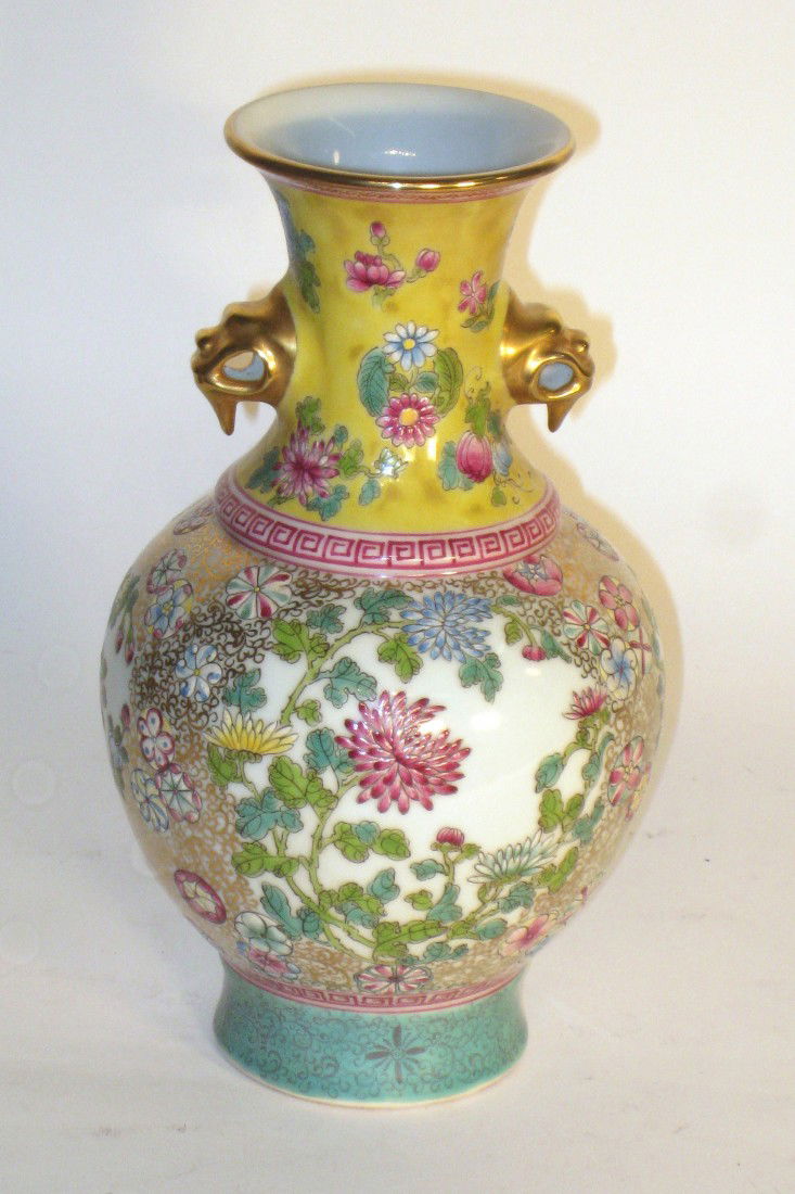 Wucai Porcelain Vase: A wucai glazed with Qianlong mark with a flared head and foot and dragon handles featuring a multitude of different flora in raised form with colors of red, blue, yellow, green luster gold. 9 1/2" in