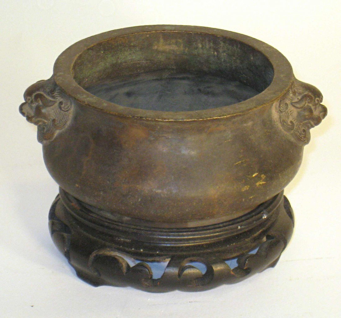 Bronze Bowl: Stands 3 1/2" high on its wooden stand , a small bronze pot with fierce dog handles. Set upon a wooden base.