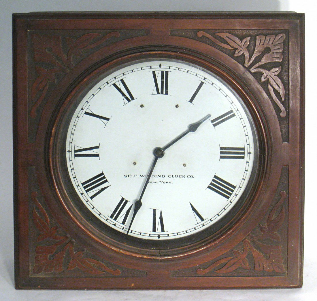 Carved Clock By Self Winding Clock Co.: A 21 1/2" square carved wood square cased wall clock whose dial is signed "Self Winding Clock Co." The Self Winding Clock Co. was formed by Charles Pratt in New York in 1886 to market their recent 188
