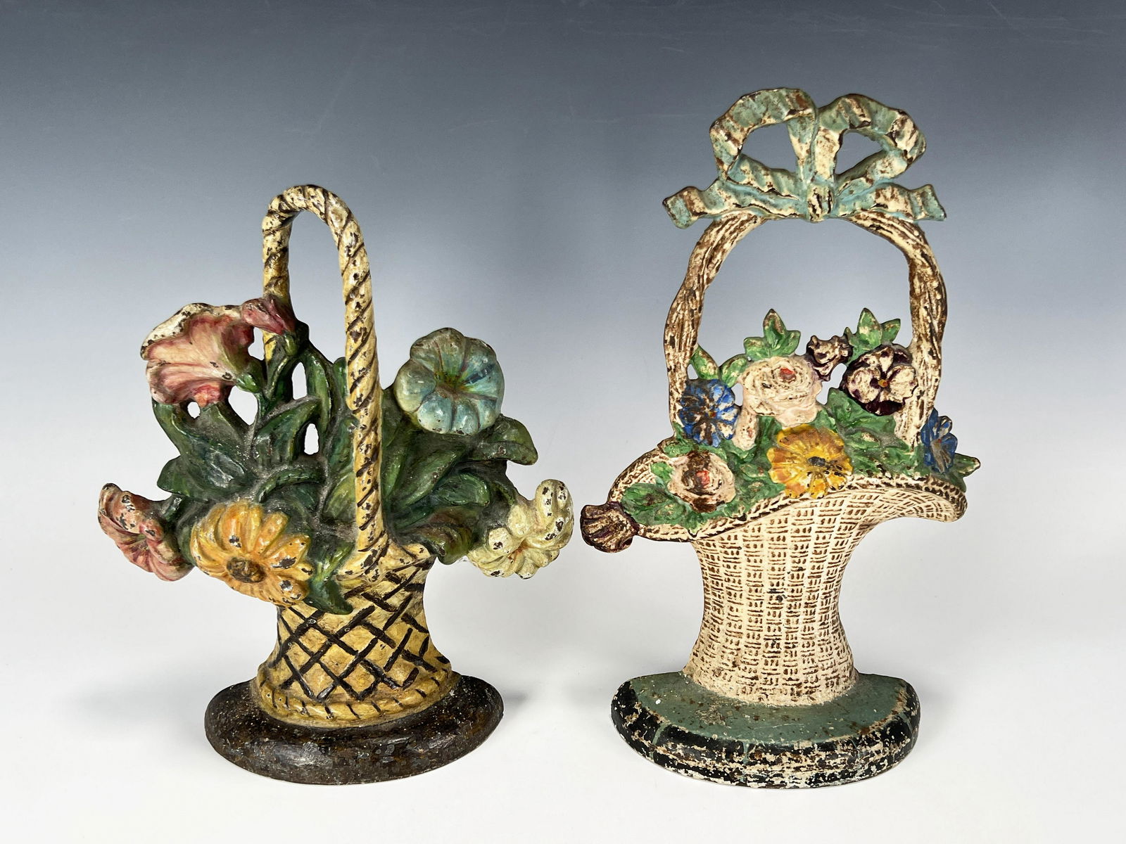 TWO FLORAL CAST IRON DOORSTOPS: TWO FLORAL CAST IRON DOORSTOPS Two handled baskets full of flowers painted in pastels. 11" x 6 3/4" x 2 1/4" Shipping:<