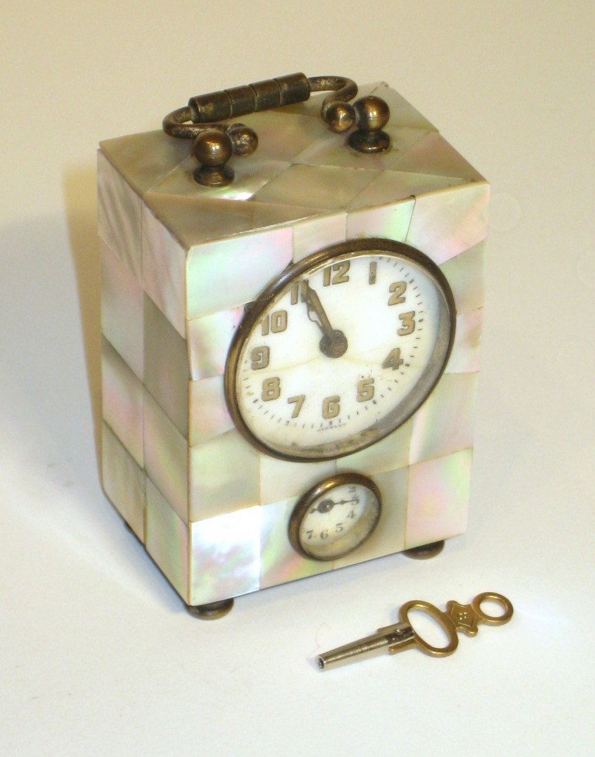 Small Desk Clock With Nacre Case: A 3" desk or "Boudoir" clock with a case covered by nacre, or mother-of-pearl. The porcelain dial, with radium,is marked "Germany" with a lower alarm feature. Brass carrying handle.