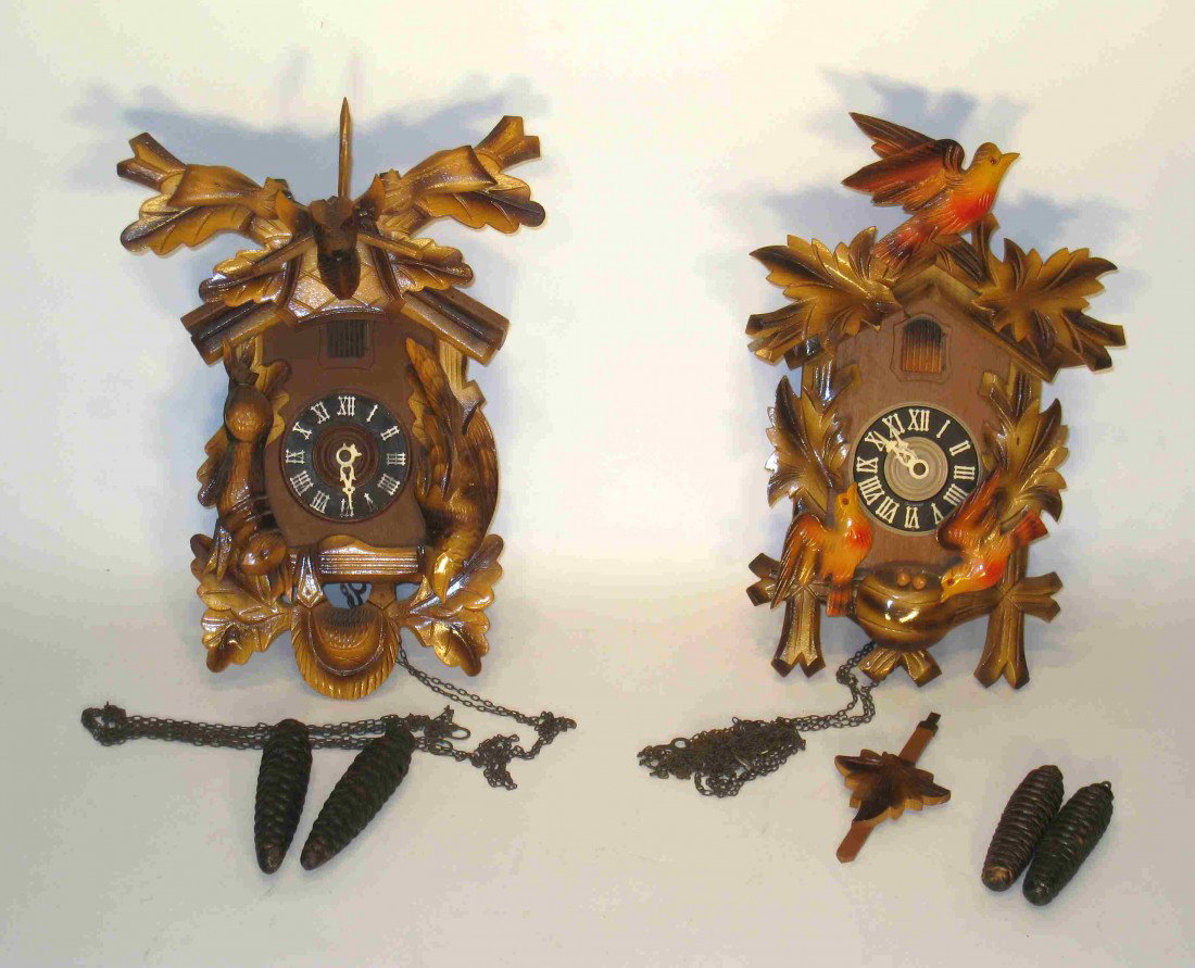 Two Cuckoo Clocks: Two carved and painted cuckoo clocks, complete with crests, weights and pendulums. Chain wind 30 hour type.