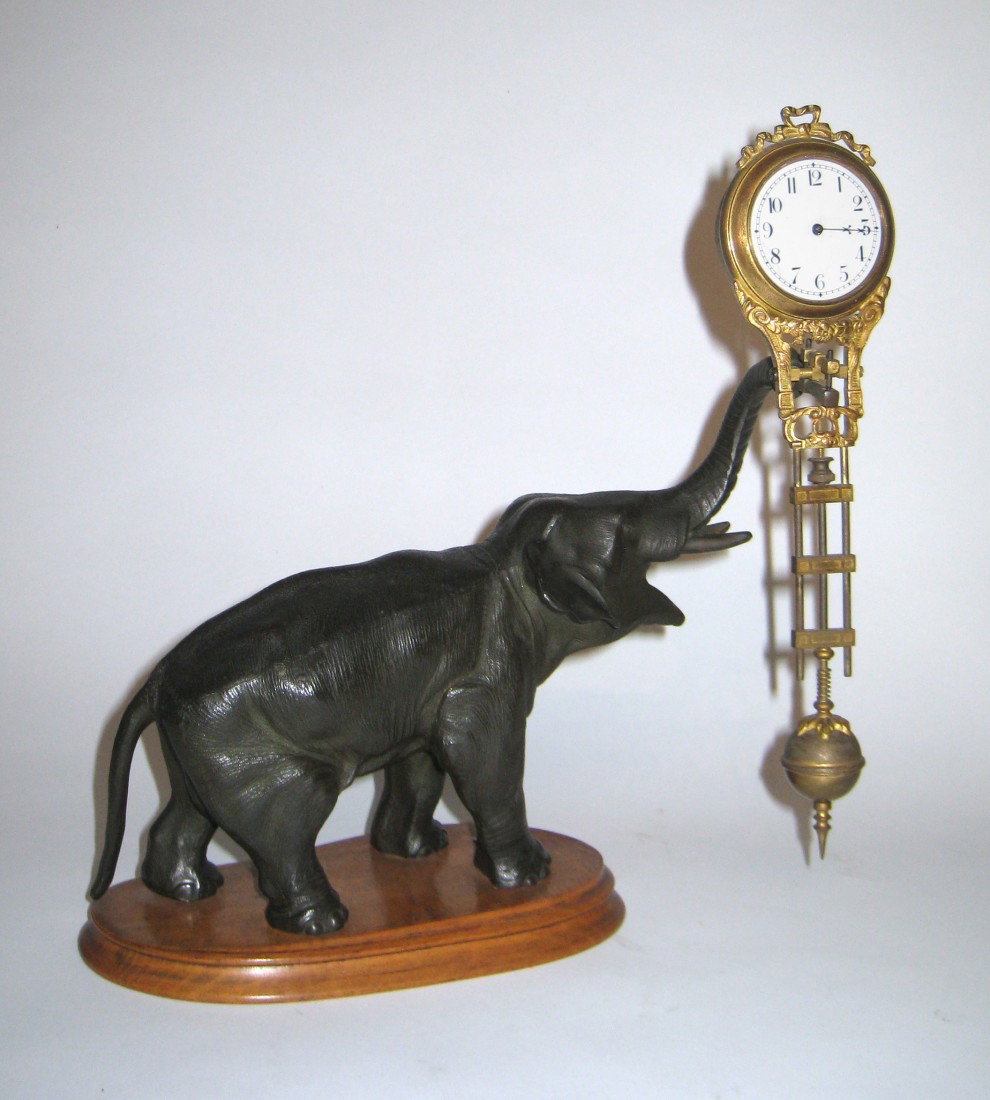 Elephant Swinger: A swinger clock by Jughans of Germany dating to the late 1800s or early 1900s, whose base is a metal casting of an elephant with her trunk raised. Lacking the glass covering the dial