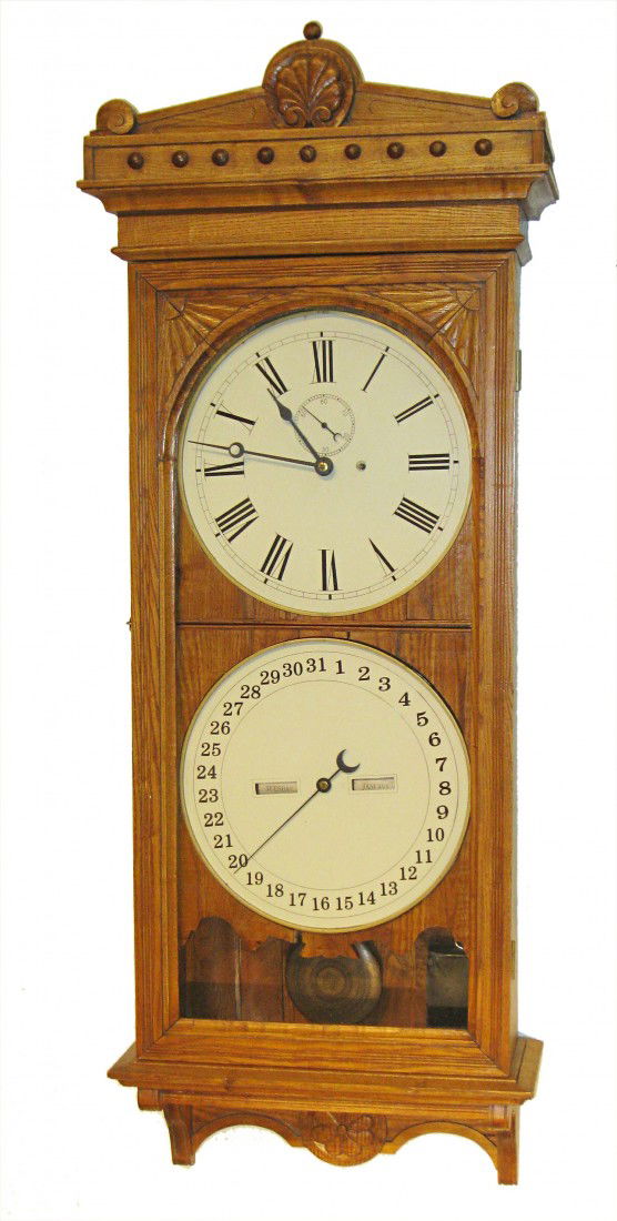 Ithaca Calendar Clock, Wall Style: A hanging wall clock in solid oak with the double dial feature, having a large and boldly displayed calendar dial below the time dial.