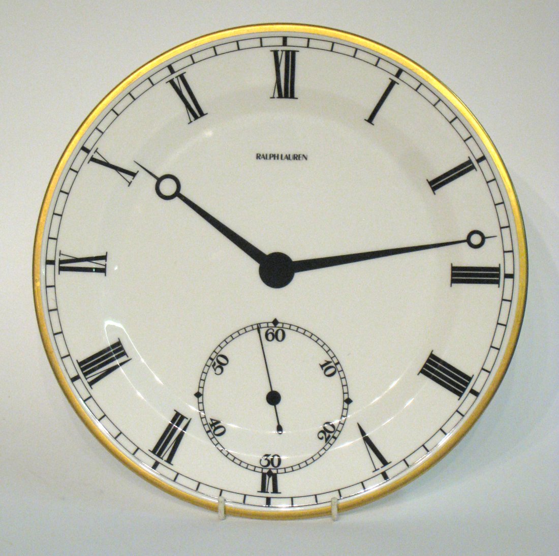 Ralph Lauren Plate In Form Of Clock Dial: Signed Ralph Lauren. Marked "Wedgewood Bone China" on back. 12 3/4" in diameter. Shipping: We are able to pack and ship this item to an address in the United States for $30.00 via USPS Priority Mail. 