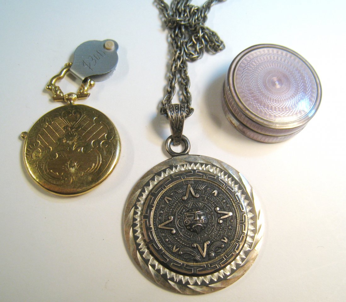 Three Items: Including a pendant possibly of Aztec style marked "Sterling", a silver enamel cylindrical pill box with severe enamel damage, and a hollow pendant of engraved gold resembling a pocket watch. Shipping