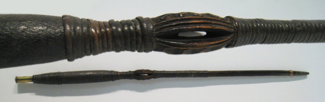 Antique African Staff: A 31" staff made from carved wood, cane, copper and a rife shell. The central area carved with a bulbous zigzag and pierced through, the handle defined with coiled cane and topped with a bullet shell 