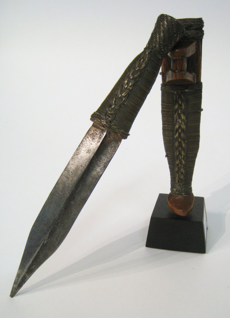 African Knife: Within a carved wood sheath with brass wire coiled and woven about, 8" in height,. with a ebonized wood base for display. Shipping: We are able to pack and ship this item to an address in the United S