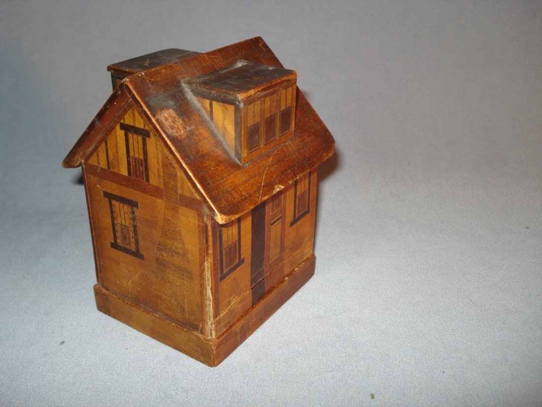 Puzzle Savings Bank: A wooden hand made and ink decorated and inlay wood savings bank in the form of a house. Coins are taken in through the roof, while opening the bank to empty the loot presents a challenging puzzle. Sh