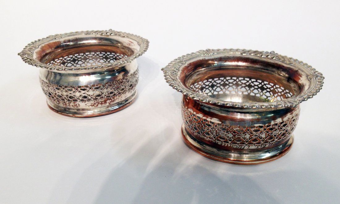 Pair Of Wine Coasters: In cylindrical form, with pierces silver plate fenders enclosing a turned wooden bottoms, 7" in diameter. Wear to silver plate. Shipping: We are able to pack and ship this item to an address in the Un