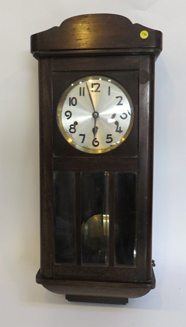 Wall Clock: A wall clock, or "box" clock, featuring w wood case with bevel glass door and convex glass bezel, metal dial with painted on numerals and striking in the "bim-bam" style. Early 20th century, 31" X 13"