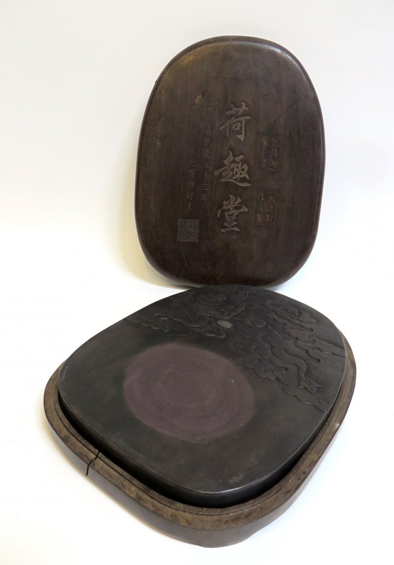 Large Duan Chinese Inkstone: An exceptionally rare and desirable Qing inkstone within a carved and fitted lidded wood casement, 14" X 11". The stone with curved sides and embossed with a five clawed dragon and flaming pearl, and
