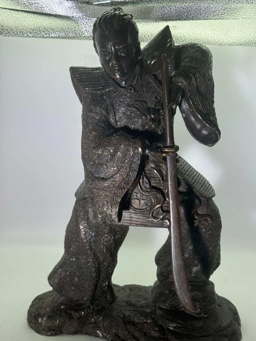 Bronze Figure of a Samurai Warrior, Japanese: A substantial cast bronze figure depicting a samurai warrior in dynamic standing pose, shown holding a drawn sword with both hands. The figure wears elaborately detailed armour and layered robes,