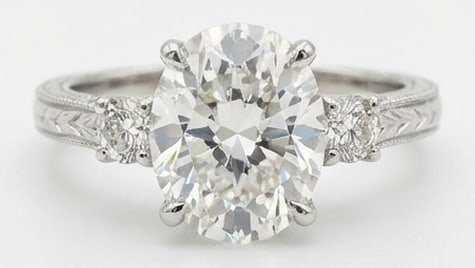 IGI Lab Grown 5.00 Ct Oval Diamond Ring – Vintage Three-Stone with Engraved Shank – / in 14K: Graceful and eye-catching, this ring is set with a 5.00 carat IGI Certificate lab grown Oval center diamond. Set in White Gold , the ring is styled with vintage three-stone with engraved shank details