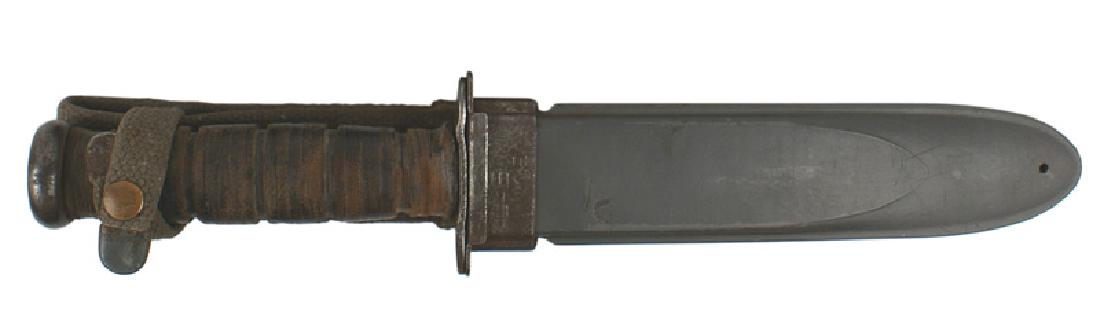 U.S. WWII Navy KA-BAR combat knife: D-098 U.S. WWII Navy KA-BAR combat knife. Flat pommel with a leather rings grip. Crossguard is marked "KA-BAR" and "USN-MK2". 7" blade is gray and shows wear. Blue-gray fiber scabbard is separating al