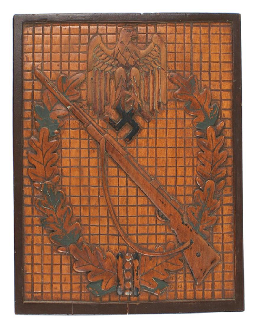 German combat Infantry Assault Badge plaque: G-042 Carved wood plaque of a German combat Infantry Assault Badge. Pronounced and well detailed relief eagle/swastika and rifle on an oak leaf wreath. Badge is carved against a squared tile effect ba