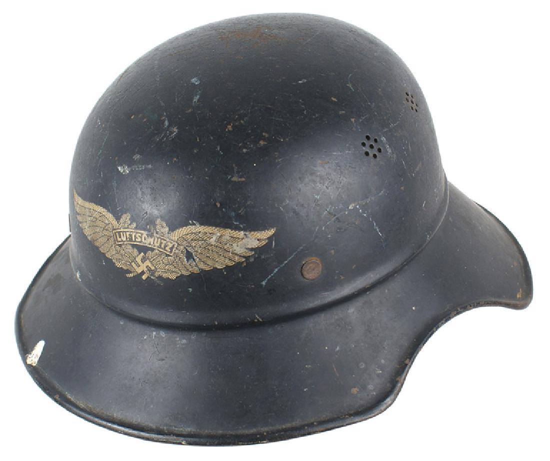 German WWII Luftschutz one-piece helmet: E-051 German Luftschutz one-piece helmet. 75% original dark blue finish with a large winged swastika and "LUFTSCHUTZ" decal on front. Missing chinstrap and drawstring liner. About II
