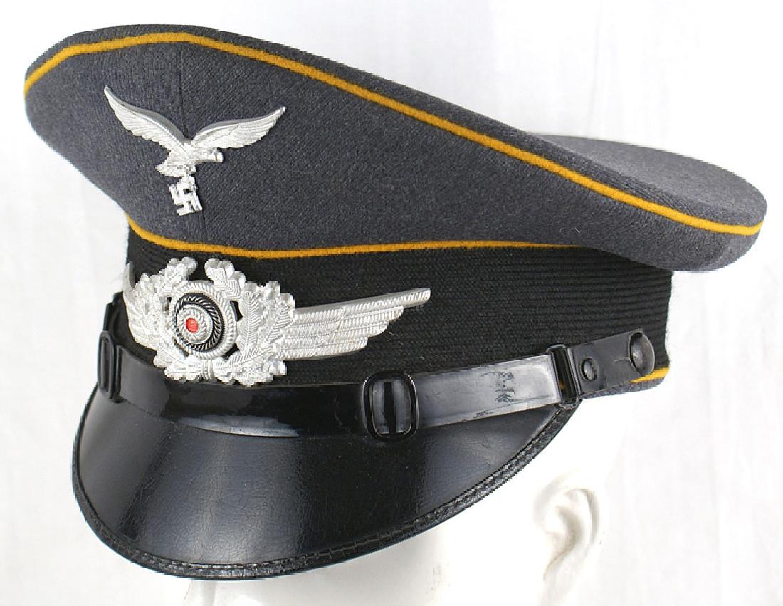 German WWII Luftwaffe EM peaked cap: E-088 Luftwaffe EM. Nice high peak, with a black band and yellow-gold piping. Metal eagle/swastika and winged wreath/rosette. "Polished" black vulcan brim and leather chinstrap. Brown leather sweatban
