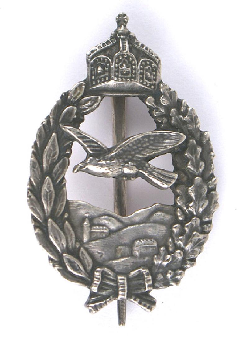 Prussian WWI Commemorative Army Pilot Badge: B-051 Prinzen size Prussian Commemorative Army Pilot's Badge. Crowned oak leaf/linden leaf wreath with a cut - out eagle flying over an aerial view of topography and buildings. Age toned silver badge.