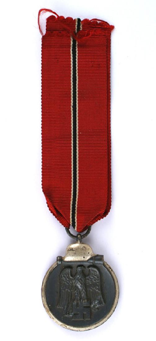 German WWII Eastern Front Medal: B-127 Eastern Front Medal. Darkened finish on a silvered perimeter with a helmet/stick grenade. Obverse bears a relief black eagle/swastika. Reverse "WINTER BATTLE IN THE EAST 1941/42". Suspension rin