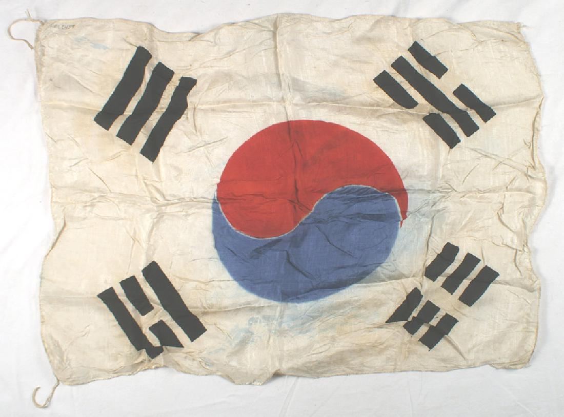 Korean War South Korean Flag: H-167 Korean War - South Korean Flag. Red/Blue "yin and yang" and black bars in corners - printed on white silk. Printed name of G.I. "HOECHST" in upper corner. Corner cord ties. 25" x 33". Age toned.