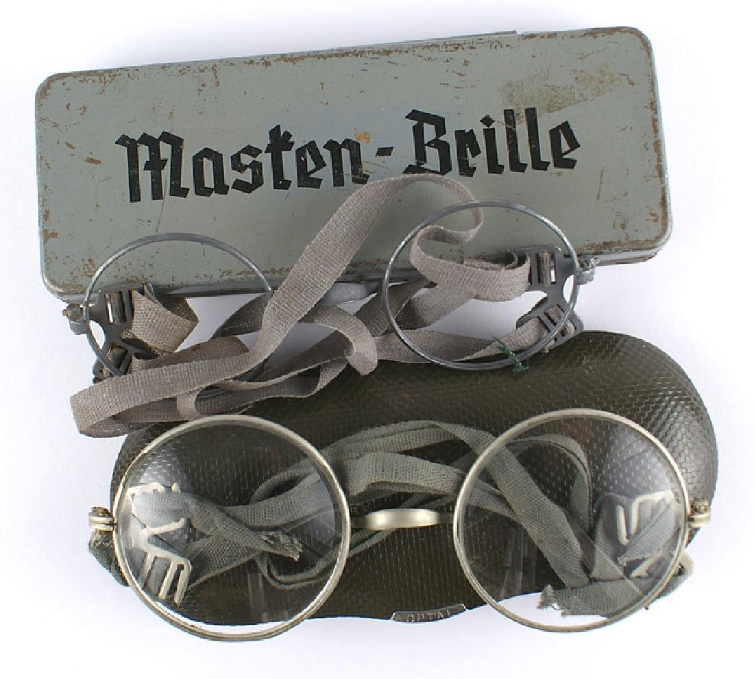 Two pairs of German WWII eyeglasses: N-010 Two pairs of German WWII eyeglasses: (1) Large round lenses/metal frame. Narrow cloth strap. Velour lined case-marked "OPTAL". (2) "Masten-Brille". Rectangular gray metal box with a hinged lid.