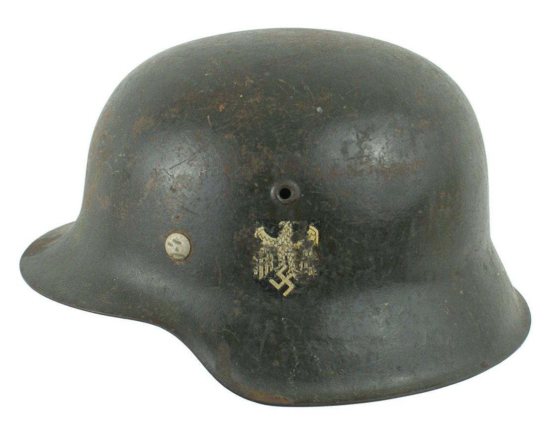 German Army M1942 single decal helmet: E-023 German Army M1942 single decal helmet. Some lighter tan camouflage visible under the 80% dark green finish. 85% eagle/swastika decal. Original leather chinstrap and brown leather drawstring line