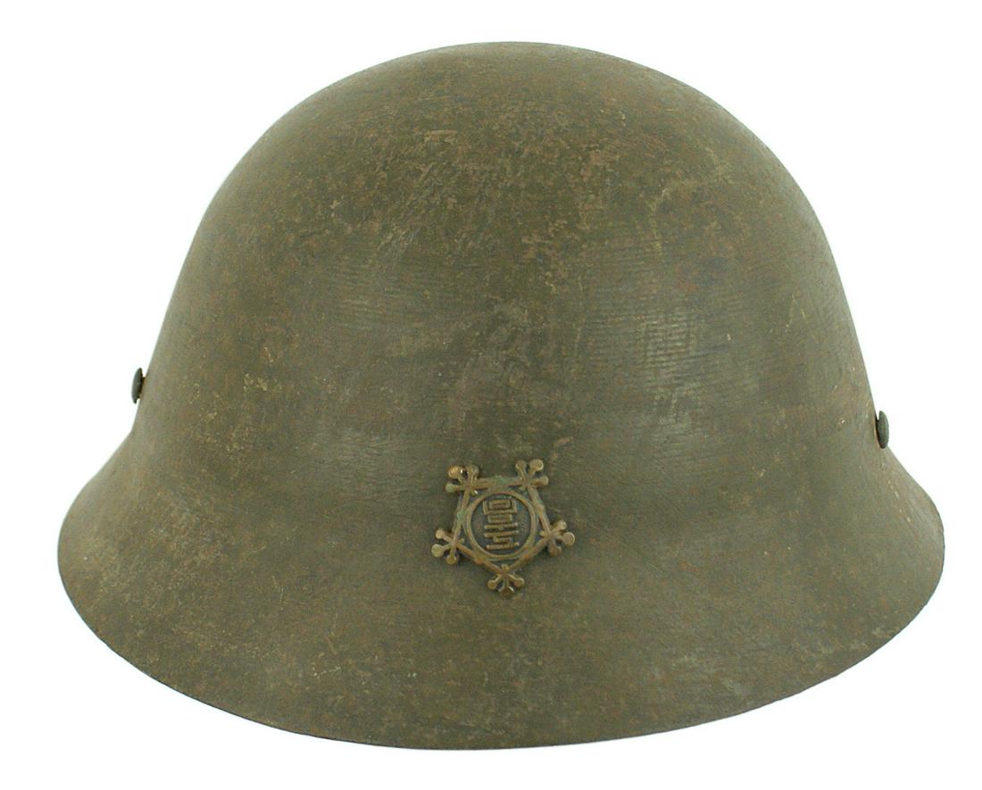 Japanese WWII helmet Variant: E-066 Japanese WWII helmet. Variant with slanted brims and sides. Badge applied to front has relief characters within a stylized frame. O.D. finish. Three rivets hold the liner band as well as the "D"