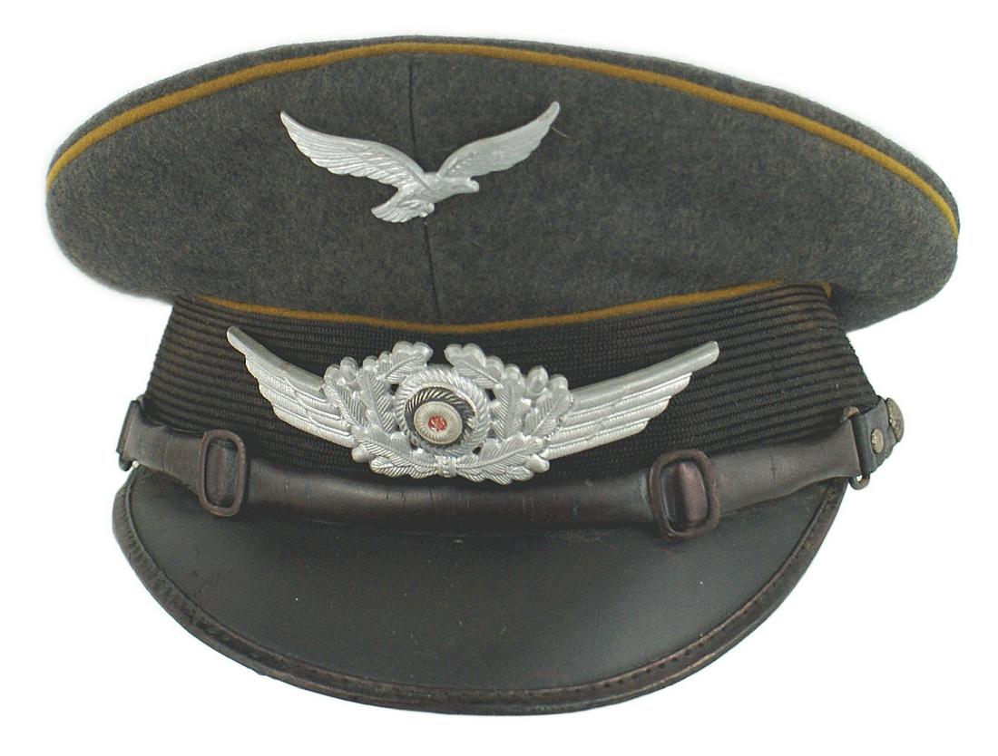 German WWII Luftwaffe EM Signal peaked cap: E-089 German WWII Luftwaffe EM Signal peaked cap. Blue - gray body with a black band and cinnamon piping. Metal flying eagle (missing swastika) and winged rosette/wreath. Dry leather chinstrap. Stiff 