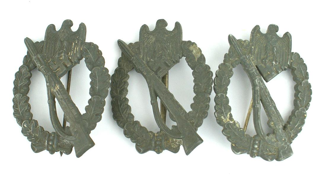 Three German WWII Infantry Assault Badges: B-055 Lot of 3 German WWII Infantry Assault Badges. Eagle/swastika at the top of an open oak leaf wreath holding a rifle with a fixed bayonet. Heavy type with good detail. Dark metal showing some trac