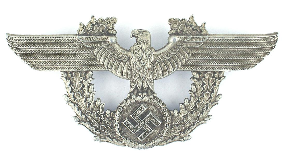 German WWII Police shako eagle frontplate: E-125 Third-Reich Police shako eagle/swastika frontplate. 3" x 6 1/4" eagle on an open top oak leaf wreath. Two screw posts on reverse. II